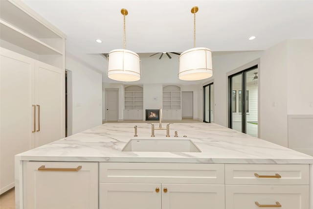 kitchen featuring open floor plan, light stone counters, recessed lighting, white cabinets, and a sink