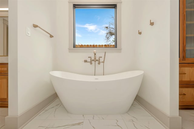 full bathroom featuring a freestanding tub, baseboards, and marble finish floor