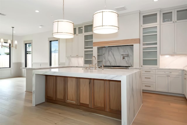 kitchen featuring visible vents, light stone countertops, a center island with sink, light wood-type flooring, and a sink