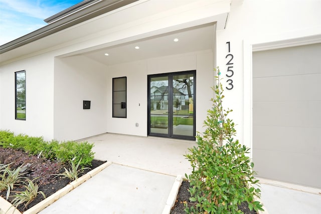 view of exterior entry with a patio area, stucco siding, and a garage