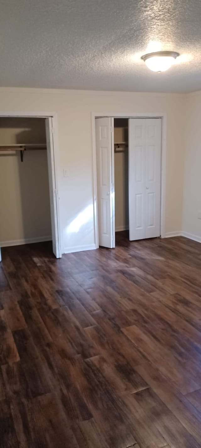 unfurnished bedroom featuring a textured ceiling, dark wood-type flooring, and multiple closets