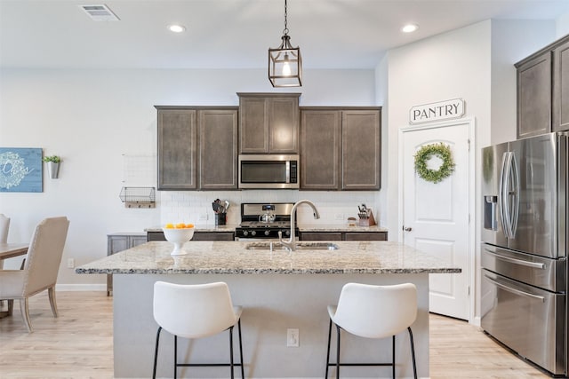 kitchen with sink, backsplash, light stone countertops, a kitchen island with sink, and appliances with stainless steel finishes