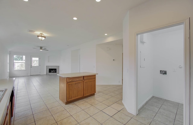 kitchen with ceiling fan, a kitchen island, light tile patterned floors, and a tiled fireplace