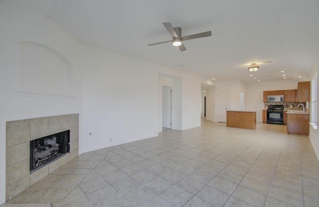 unfurnished living room with a tiled fireplace, ceiling fan, sink, and light tile patterned flooring