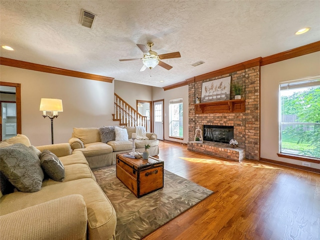 living room featuring ceiling fan, hardwood / wood-style floors, a textured ceiling, a fireplace, and ornamental molding