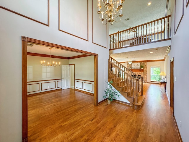 stairway with wood-type flooring, ornamental molding, a notable chandelier, and a high ceiling