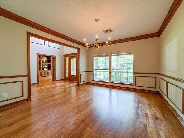 unfurnished room with a textured ceiling, light hardwood / wood-style floors, an inviting chandelier, and crown molding