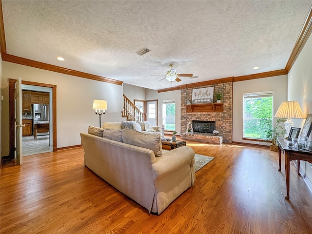 living room with ceiling fan, light wood-type flooring, a fireplace, ornamental molding, and a textured ceiling