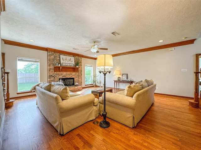 living room with a textured ceiling, light hardwood / wood-style floors, a brick fireplace, and ceiling fan