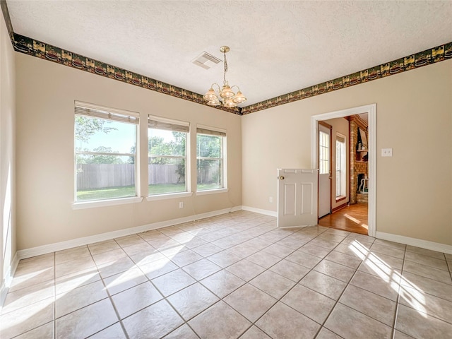 spare room with a chandelier, light tile patterned floors, a textured ceiling, and a brick fireplace