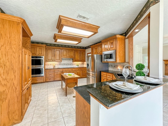 kitchen with sink, kitchen peninsula, dark stone counters, a textured ceiling, and appliances with stainless steel finishes