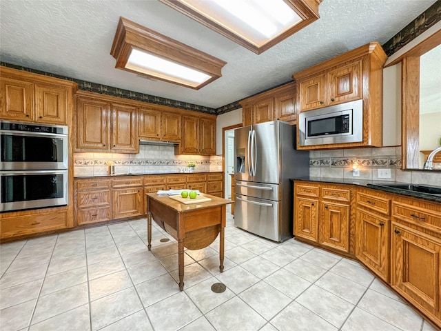 kitchen with backsplash, sink, a textured ceiling, light tile patterned flooring, and stainless steel appliances