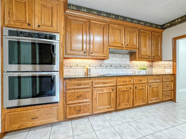 kitchen featuring light stone countertops, a textured ceiling, light tile patterned floors, tasteful backsplash, and stainless steel double oven