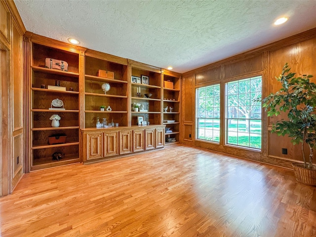 unfurnished living room with wood walls, built in features, a textured ceiling, and light hardwood / wood-style flooring