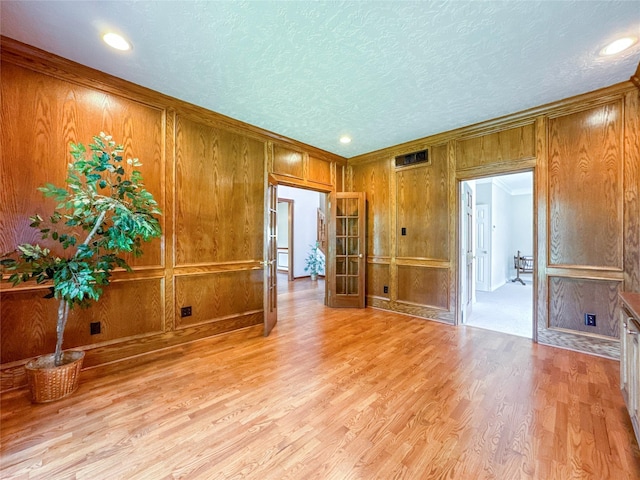 empty room featuring french doors, crown molding, light hardwood / wood-style flooring, and a textured ceiling