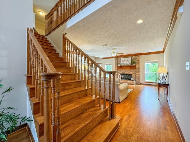 staircase featuring hardwood / wood-style flooring, ceiling fan, ornamental molding, a fireplace, and a textured ceiling