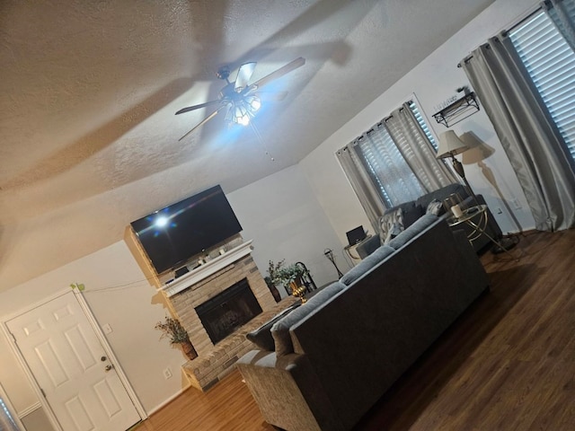 living room featuring ceiling fan, wood-type flooring, a textured ceiling, and a brick fireplace