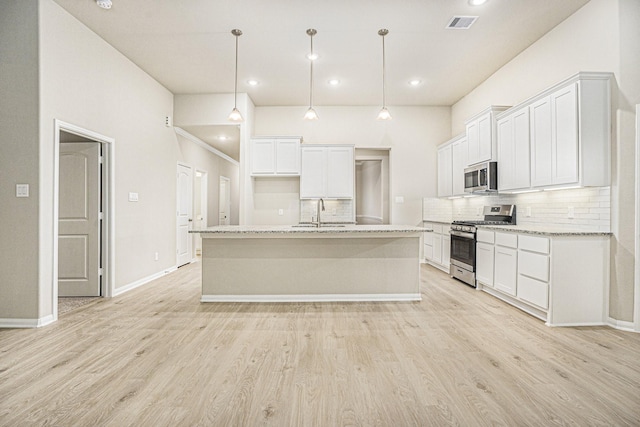 kitchen featuring appliances with stainless steel finishes, tasteful backsplash, decorative light fixtures, white cabinetry, and an island with sink