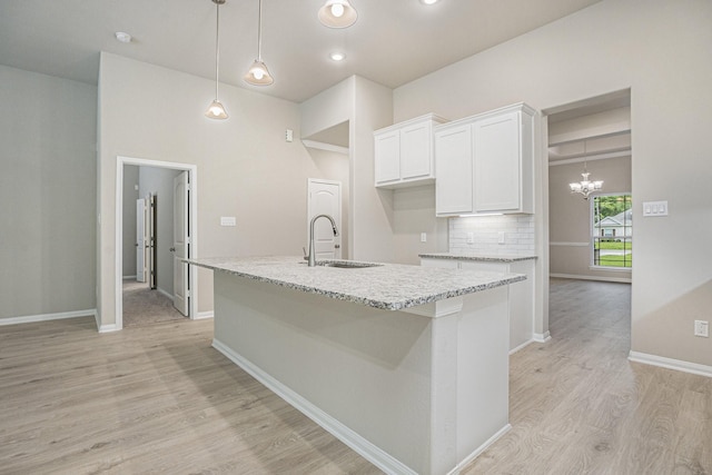 kitchen with white cabinets, light stone countertops, a kitchen island with sink, and sink