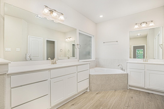 bathroom with hardwood / wood-style floors, vanity, and tiled bath