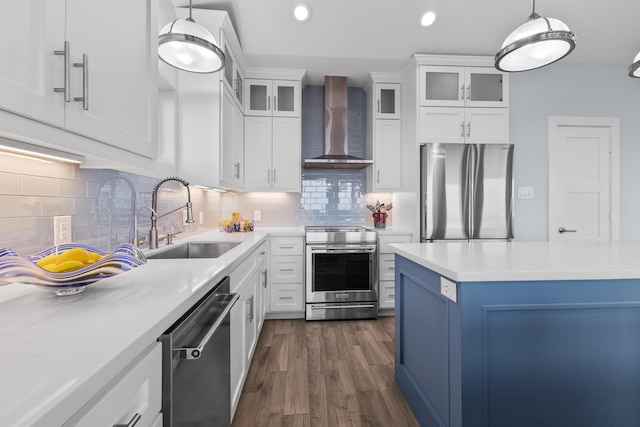 kitchen with sink, wall chimney exhaust hood, hanging light fixtures, white cabinets, and appliances with stainless steel finishes