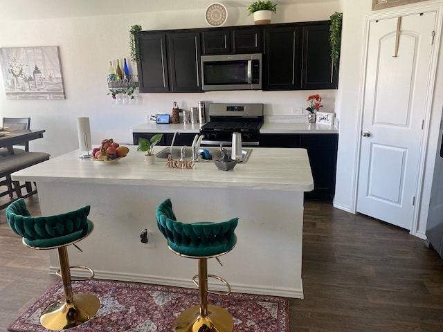 kitchen with dark hardwood / wood-style flooring, sink, stainless steel appliances, and a kitchen island with sink