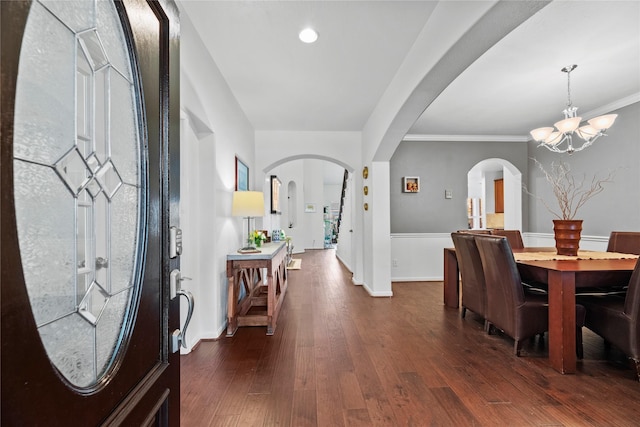 entryway with ornamental molding, dark wood-type flooring, and a notable chandelier