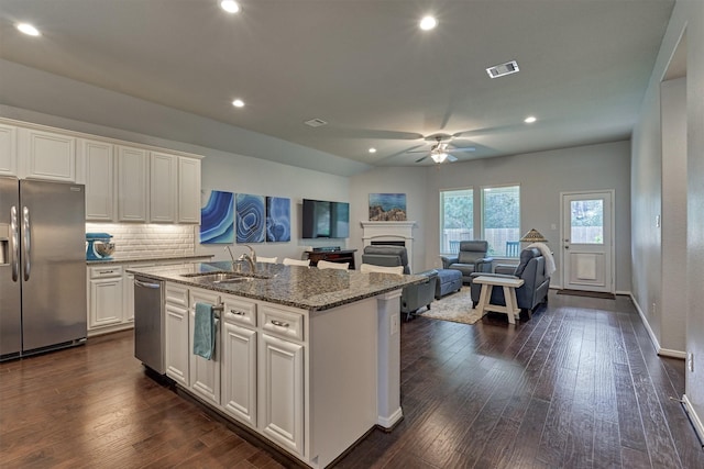 kitchen with light stone countertops, appliances with stainless steel finishes, sink, a center island with sink, and white cabinets