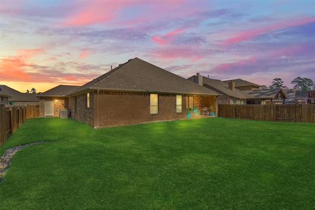 back house at dusk with a yard and central AC unit