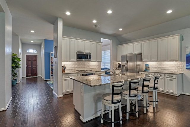 kitchen with white cabinets, appliances with stainless steel finishes, a kitchen breakfast bar, and an island with sink