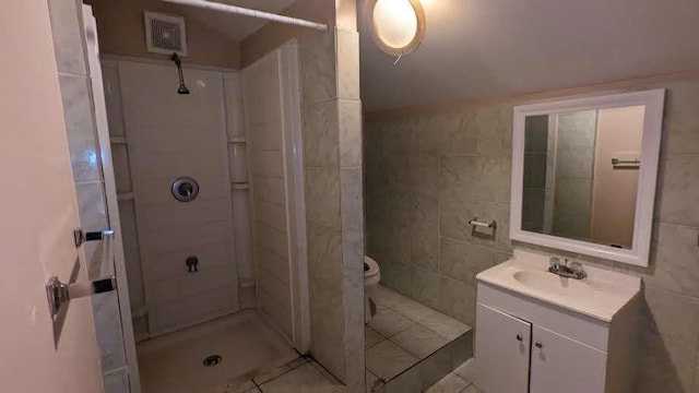 bathroom featuring tile patterned flooring, toilet, tiled shower, vanity, and tile walls