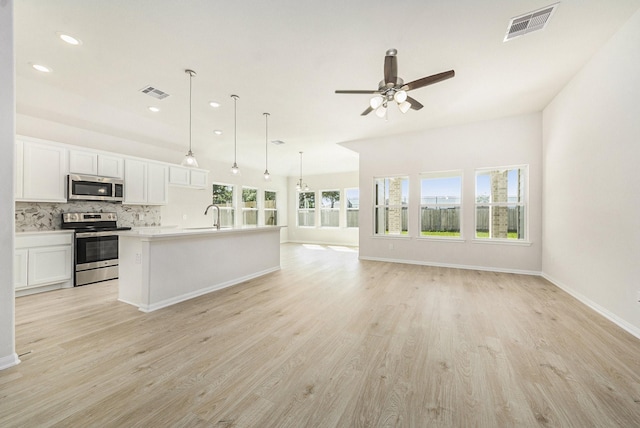 kitchen featuring appliances with stainless steel finishes, backsplash, a kitchen island with sink, white cabinetry, and hanging light fixtures