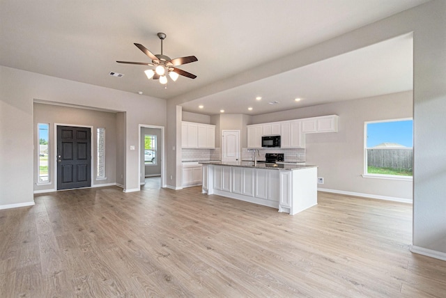 kitchen with light wood-type flooring, ceiling fan, black appliances, a center island with sink, and white cabinetry