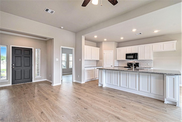 kitchen with light wood-type flooring, light stone counters, ceiling fan, sink, and white cabinetry