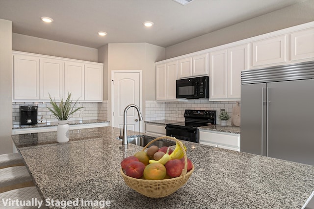 kitchen with a kitchen island with sink, black appliances, sink, dark stone countertops, and white cabinetry