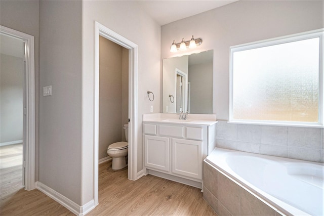 bathroom featuring hardwood / wood-style flooring, a relaxing tiled tub, toilet, and vanity