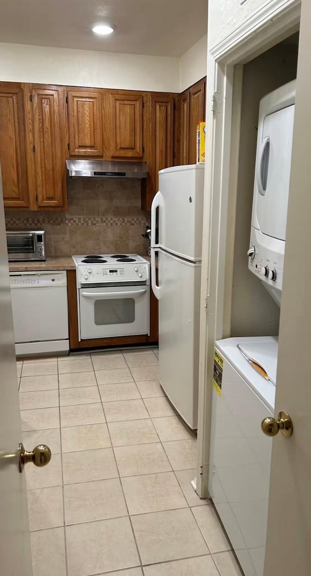 kitchen featuring decorative backsplash, white appliances, light tile patterned floors, and stacked washer and clothes dryer