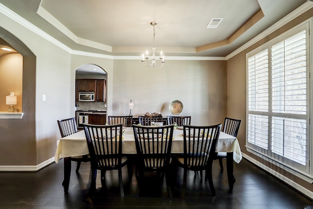 dining room with dark hardwood / wood-style floors, a raised ceiling, ornamental molding, and an inviting chandelier