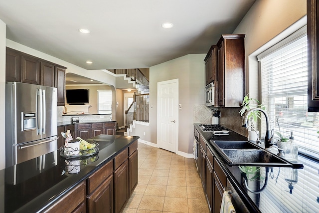 kitchen with backsplash, sink, light tile patterned floors, dark brown cabinets, and stainless steel appliances