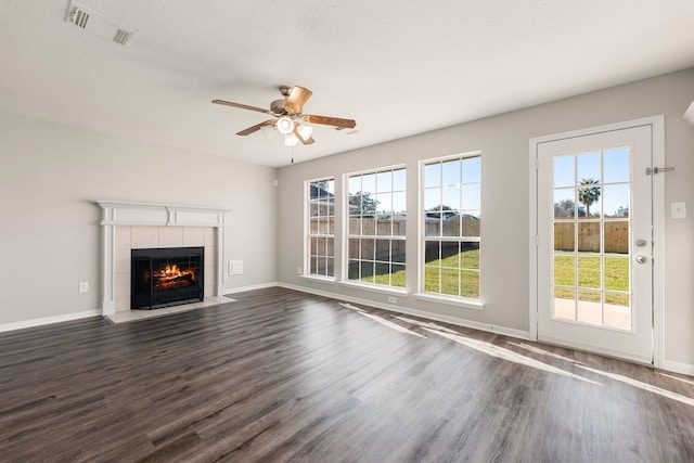 unfurnished living room featuring a tiled fireplace, ceiling fan, plenty of natural light, and dark wood-type flooring