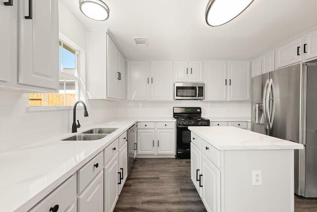 kitchen with light stone countertops, stainless steel appliances, sink, white cabinets, and a center island