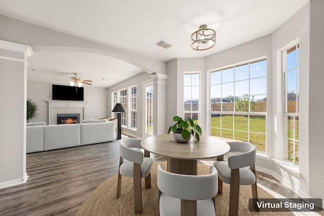 dining space featuring a fireplace, wood-type flooring, ornate columns, and ceiling fan