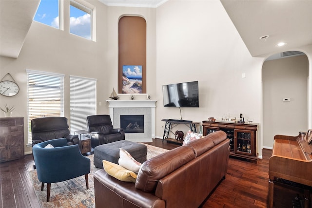 living room with a towering ceiling, dark wood-type flooring, and a tile fireplace