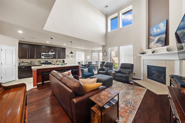 living room with a tile fireplace, a towering ceiling, and dark hardwood / wood-style floors