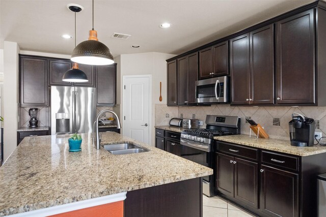 kitchen with sink, an island with sink, appliances with stainless steel finishes, tasteful backsplash, and dark brown cabinets