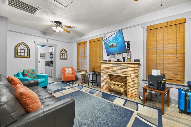 living room featuring wood-type flooring, a textured ceiling, a brick fireplace, and ceiling fan