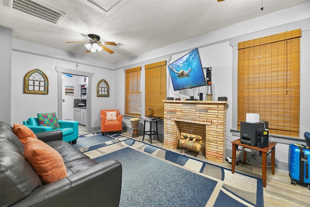 living area featuring visible vents, a ceiling fan, a fireplace with flush hearth, a textured ceiling, and wood finished floors