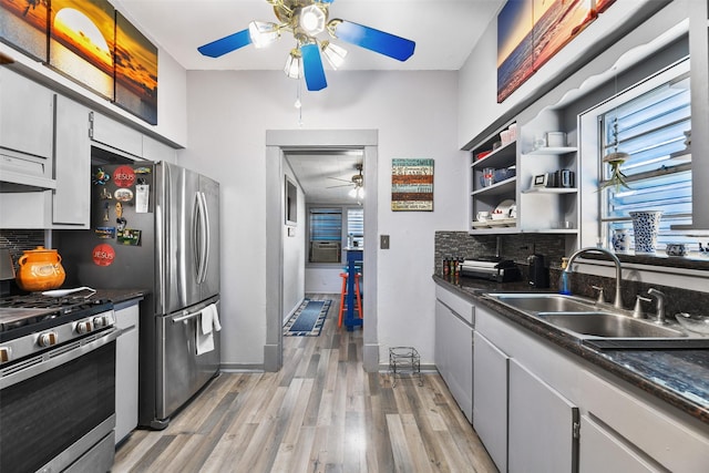 kitchen with a sink, stainless steel gas range, light wood finished floors, dark countertops, and tasteful backsplash