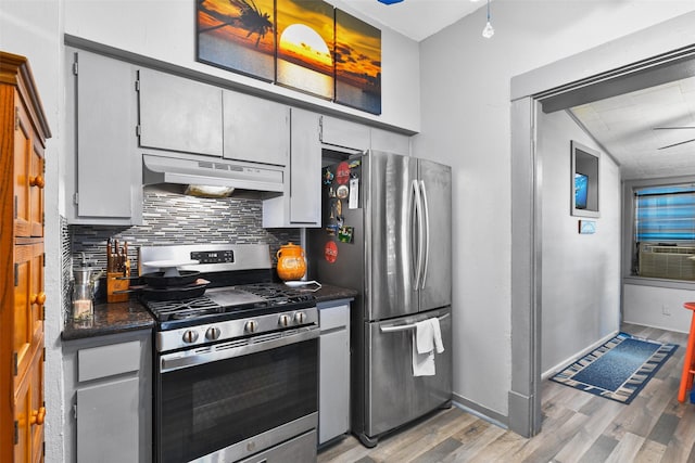 kitchen featuring dark countertops, appliances with stainless steel finishes, light wood-type flooring, under cabinet range hood, and backsplash