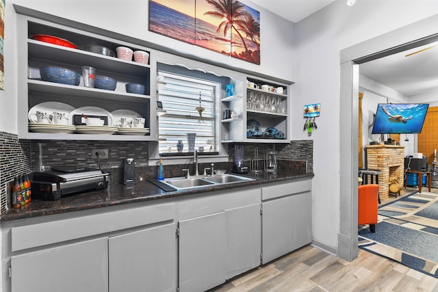 kitchen with light wood-type flooring, a sink, open shelves, and decorative backsplash